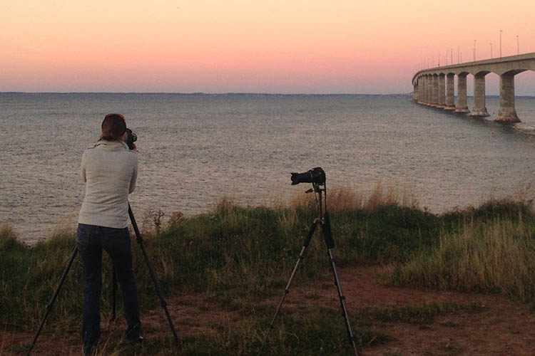 A woman take a picture of the Confederation Bridge near sunset