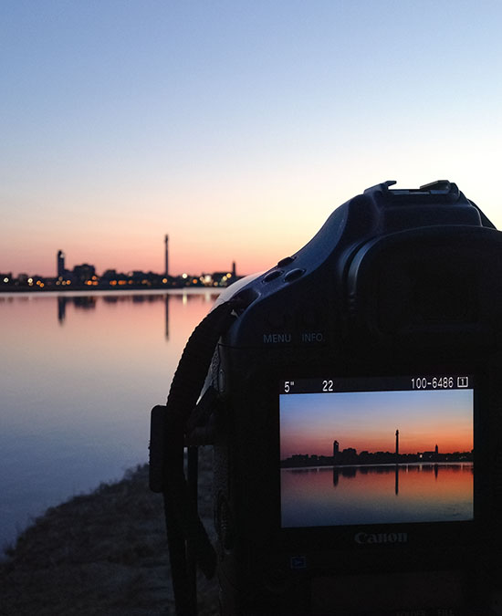 A camera in front of a city skyline at sunset with a picture of the skyline visible in the LCD display on the rear of the camera.