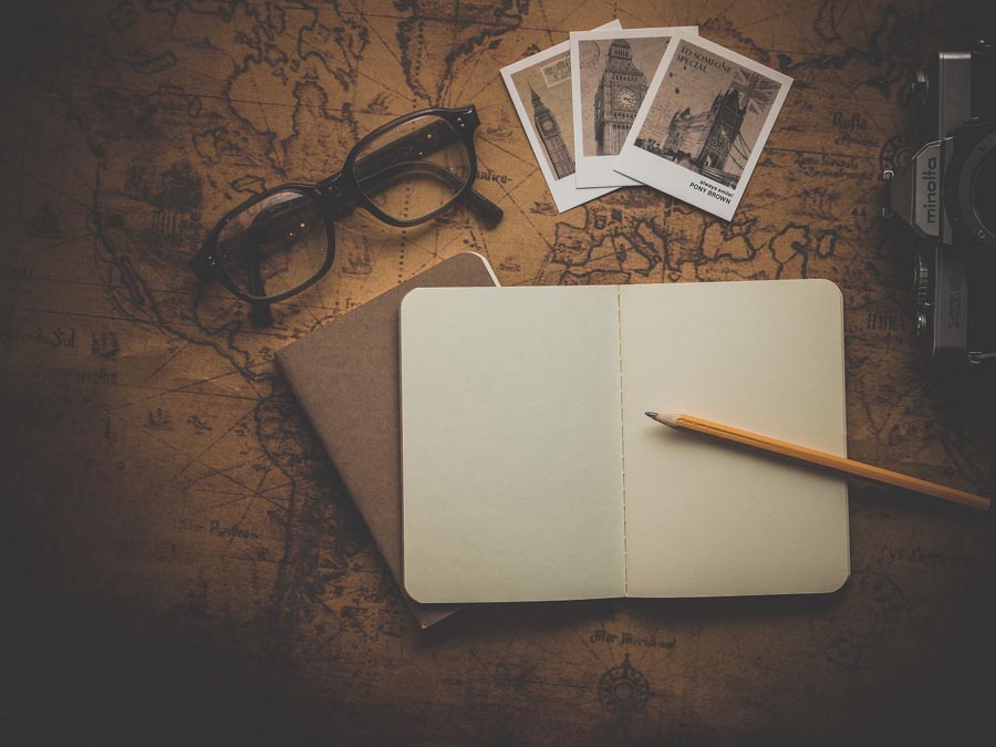An image of a notebook, pencil, eyeglasses, a camera, and several photographs sitting on top of an old-fashioned map. Image by Dariusz Sankowski from Pixabay